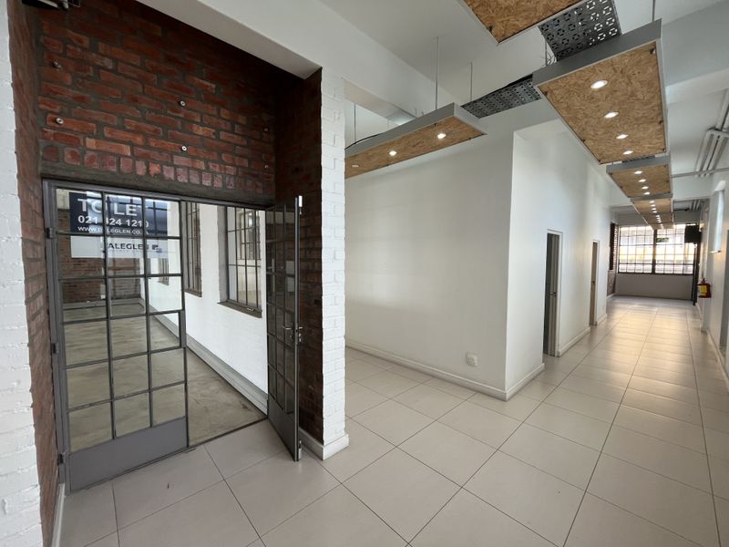 Modern industrial-style office hallway featuring exposed brickwork, tiled floors, and suspended ceiling panels with recessed lighting.