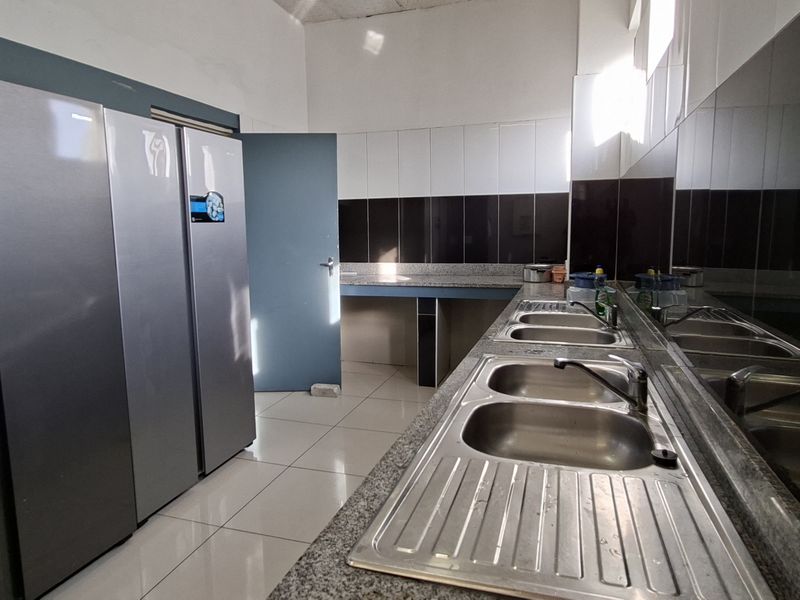 A functional scullery area featuring granite countertops, a double stainless steel sink, and tiled splashbacks, providing ample space for food preparation and cleaning.