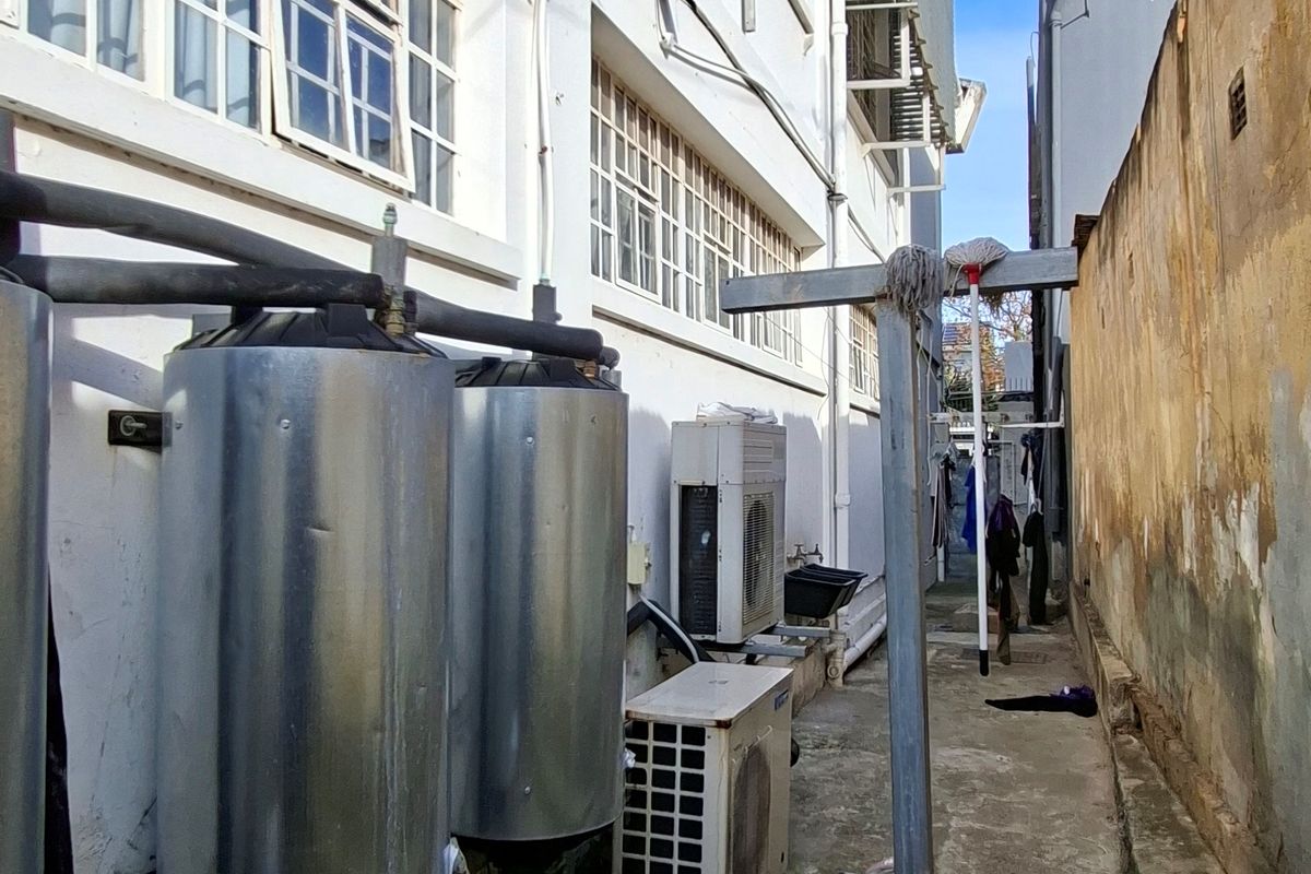 Rear exterior utility area featuring external geysers, air conditioning units, and concrete flooring with visible weathering on the building facade.