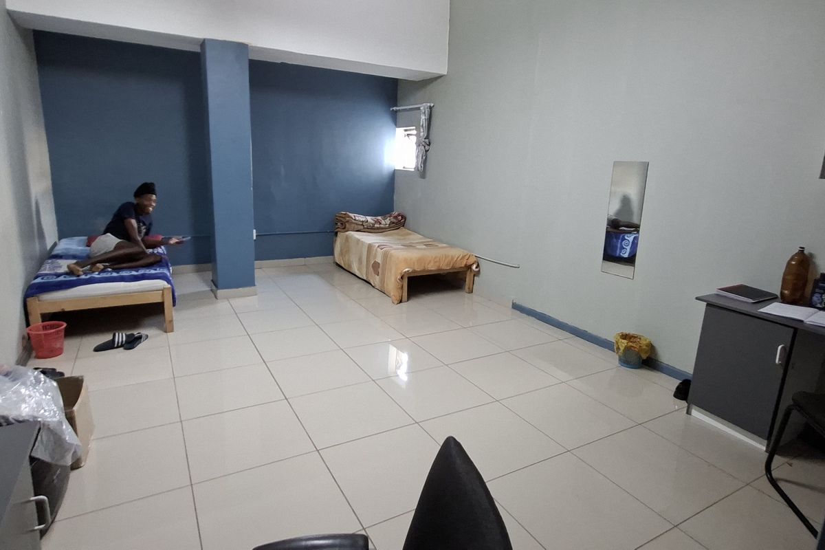 A spacious bedroom featuring tiled flooring, a structural column, and built-in wall shelving, offering a functional layout for multiple occupants.