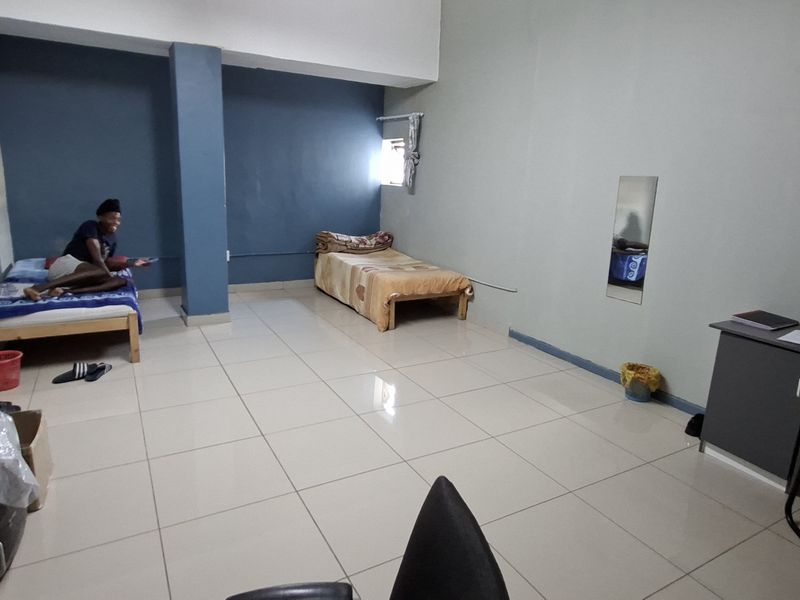 A spacious bedroom featuring tiled flooring, a structural column, and built-in wall shelving, offering a functional layout for multiple occupants.