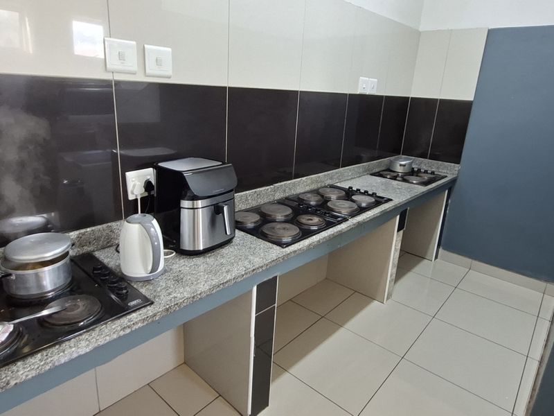 A functional kitchen area featuring granite countertops, tiled splashbacks, and multiple built-in electric hobs, providing ample workspace for cooking.