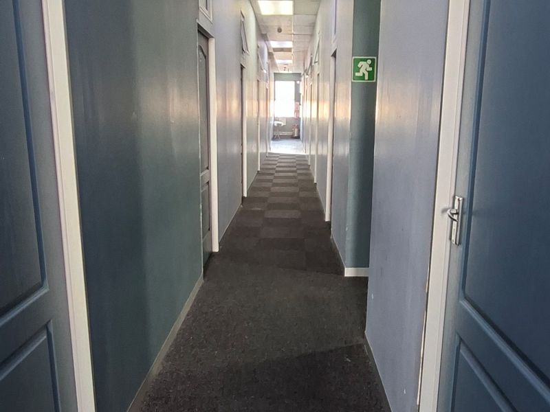 A long apartment building hallway featuring a suspended ceiling, recessed lighting, and emergency exit signage.