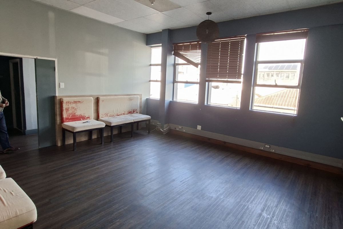 Spacious living area featuring laminate flooring, large windows with timber blinds, and a drop ceiling. The room requires cosmetic updates to improve its overall condition.