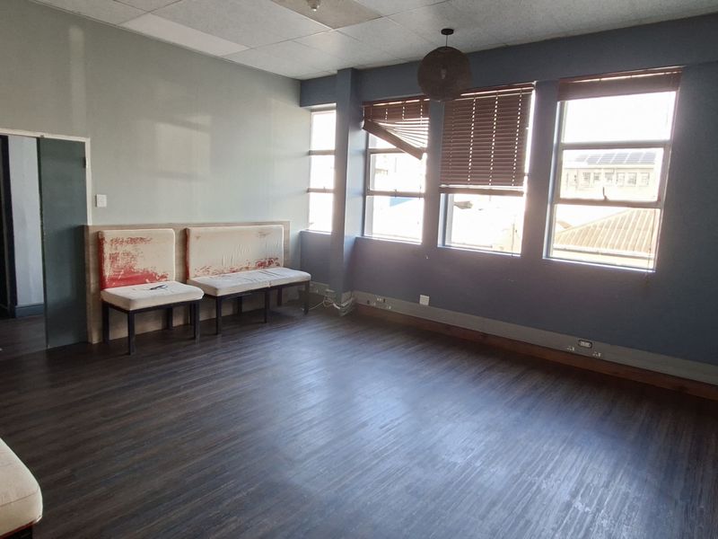 Spacious living area featuring laminate flooring, large windows with timber blinds, and a drop ceiling. The room requires cosmetic updates to improve its overall condition.