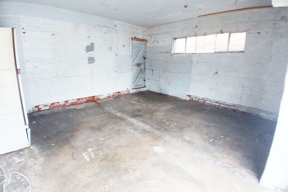 An empty utility or storage space featuring concrete flooring, exposed brickwork, and a security-grille window, suitable for renovation or workshop use.