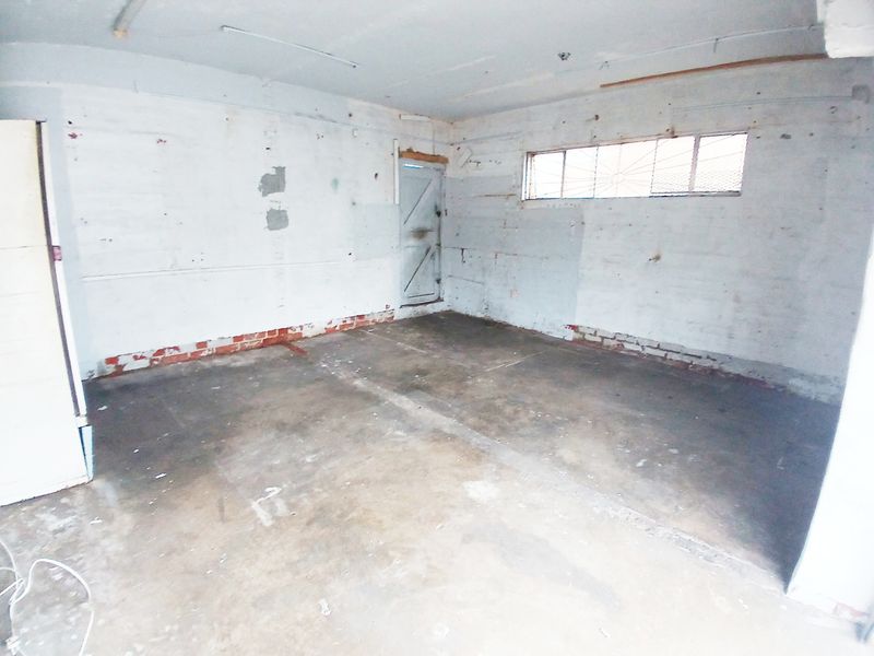 An empty utility or storage space featuring concrete flooring, exposed brickwork, and a security-grille window, suitable for renovation or workshop use.