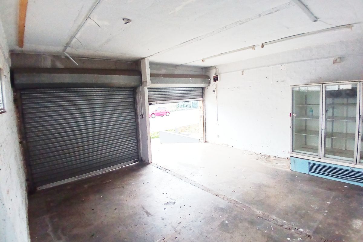 An empty retail space featuring concrete flooring, roller shutter doors, and built-in display refrigeration, requiring cosmetic refurbishment.