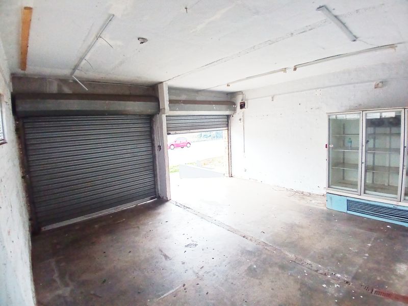 An empty retail space featuring concrete flooring, roller shutter doors, and built-in display refrigeration, requiring cosmetic refurbishment.