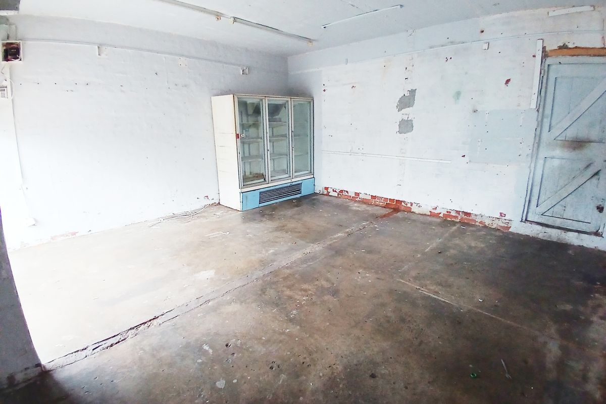 An empty utility or storage space featuring concrete flooring, exposed brick walls, and a timber door, requiring significant refurbishment and cosmetic updates.