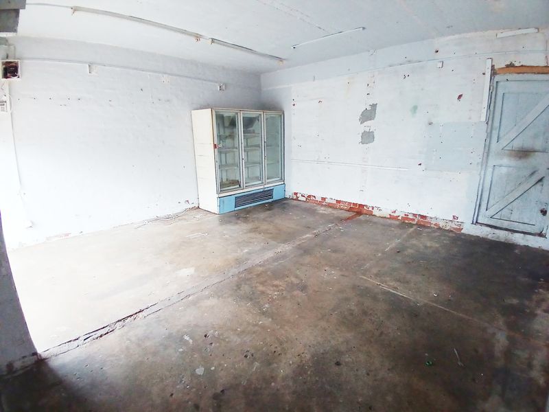 An empty utility or storage space featuring concrete flooring, exposed brick walls, and a timber door, requiring significant refurbishment and cosmetic updates.