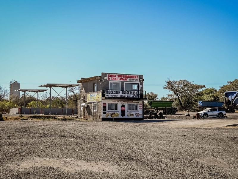 Exterior view of a commercial truck stop facility featuring a two-story building with a supermarket, take-away, and truck wash services on a gravel lot.