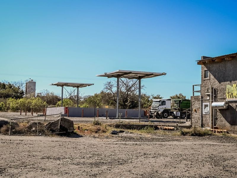 Exterior view of a commercial fuel station site featuring metal fuel canopies, a concrete forecourt, and an adjacent masonry building structure.