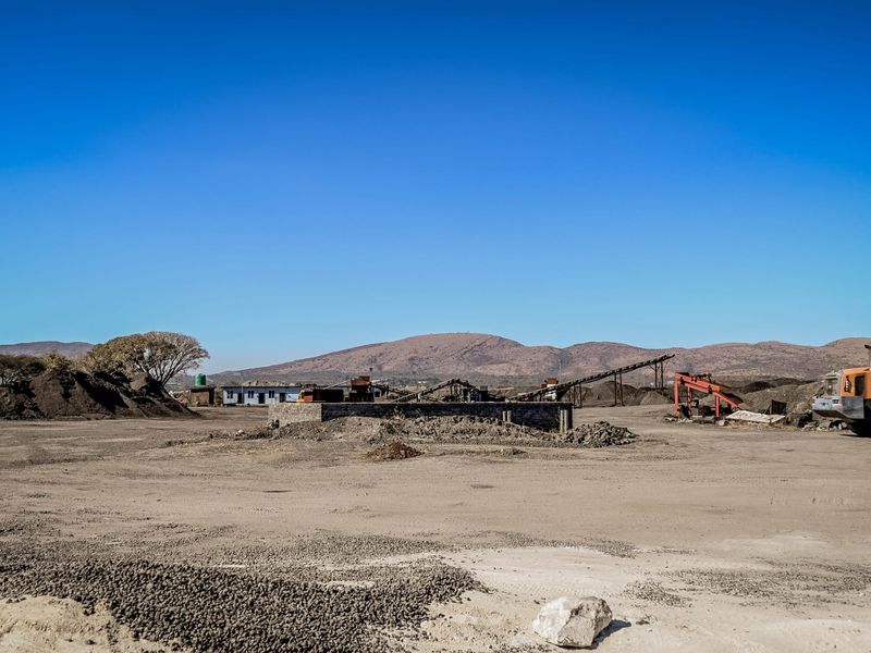 Wide view of an industrial site featuring heavy machinery, conveyor systems, and large material storage piles in an open yard setting.