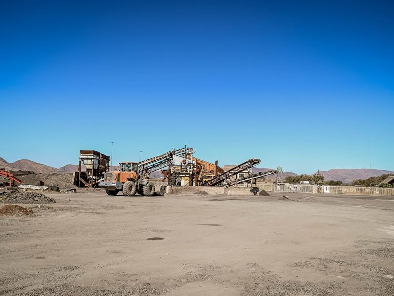 Industrial site featuring a large-scale crushing and conveyor plant set within a spacious, unpaved yard area.