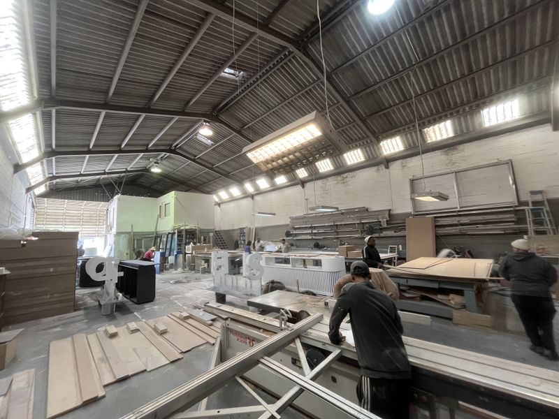 Spacious industrial workshop featuring high exposed steel roof trusses, concrete flooring, and functional high-bay lighting, suitable for manufacturing or storage operations.