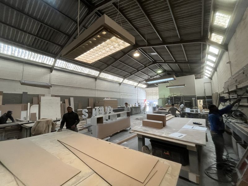 Spacious industrial workshop featuring high exposed steel roof trusses, clerestory windows for natural light, and functional overhead fluorescent lighting.
