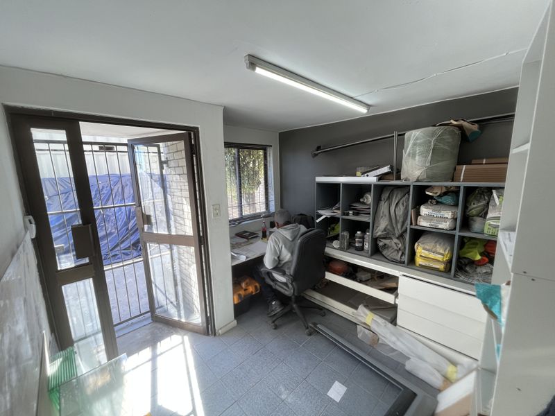 A functional office space featuring tiled flooring, built-in storage shelving, and direct access to an exterior area through a security gate.