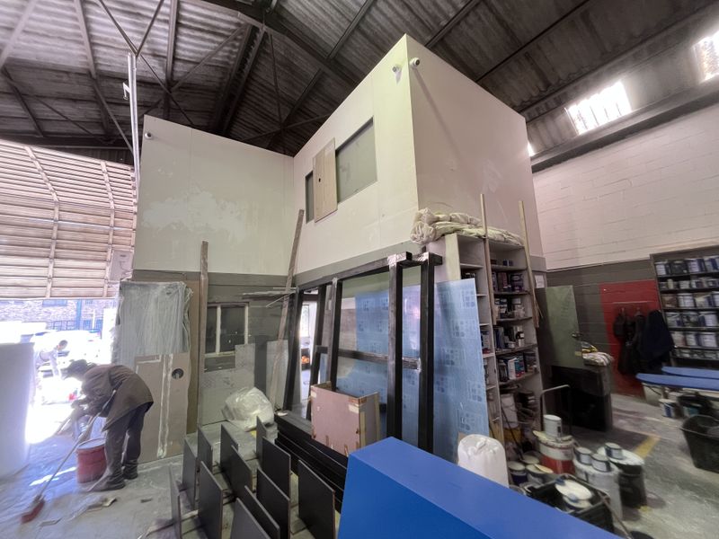 Industrial warehouse space featuring high ceilings with exposed steel trusses, a mezzanine office structure, and large roller shutter door access.
