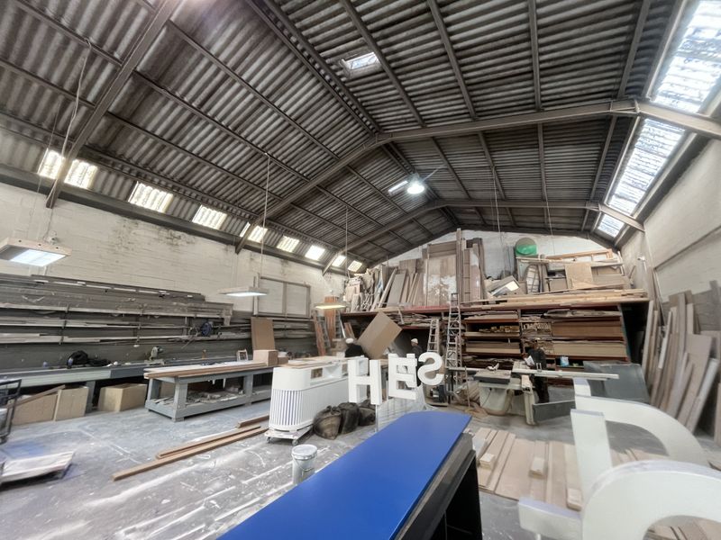 Spacious industrial workshop featuring high corrugated metal ceilings, exposed steel trusses, integrated skylights, and extensive built-in storage shelving.