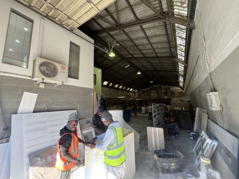 Industrial warehouse space featuring high ceilings with exposed steel trusses, skylights, and concrete block walls, currently utilized as a workshop area.
