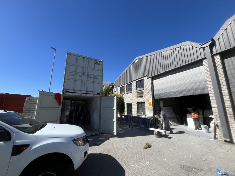Industrial warehouse exterior featuring a roller shutter door, brick facade, and paved yard area suitable for loading and logistics operations.