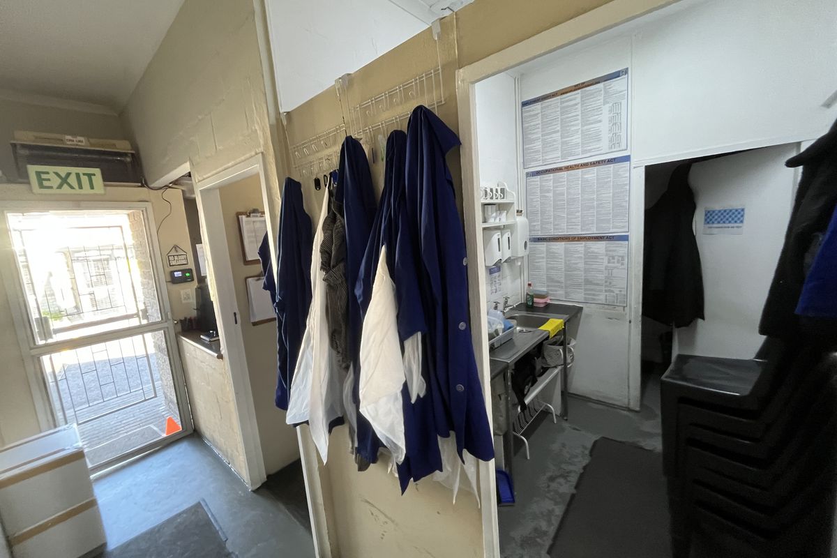 A functional utility and wash-up area featuring a stainless steel sink, security door access, and practical storage space for workplace essentials.