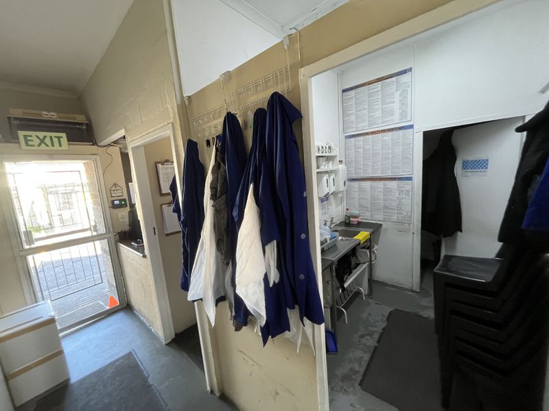 A functional utility and wash-up area featuring a stainless steel sink, security door access, and practical storage space for workplace essentials.