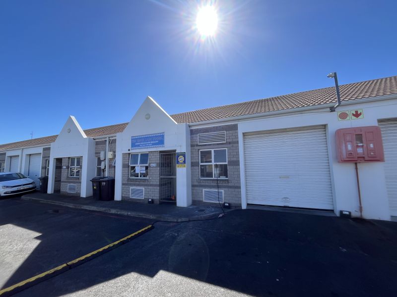 Front elevation of a commercial business unit featuring roller shutter doors, brick masonry, and a tiled roof in a well-maintained industrial park setting.