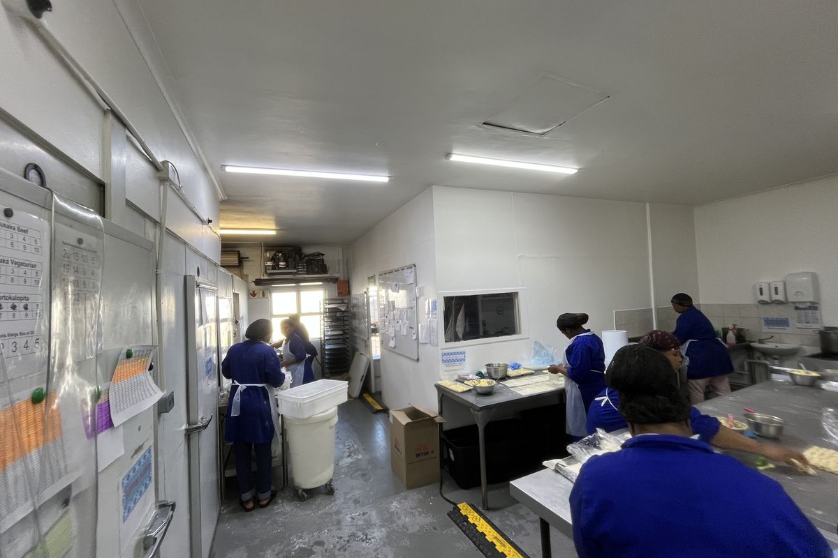 A functional commercial kitchen workspace featuring stainless steel prep surfaces, industrial lighting, and integrated cold storage access.