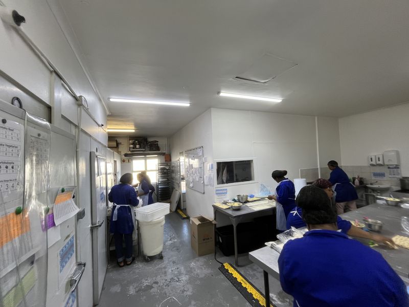 A functional commercial kitchen workspace featuring stainless steel prep surfaces, industrial lighting, and integrated cold storage access.