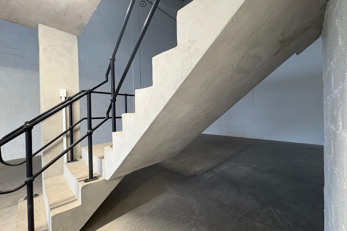 An industrial-style interior space featuring a raw concrete staircase with a black metal handrail and polished concrete flooring.