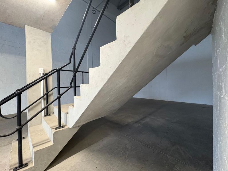 An industrial-style interior space featuring a raw concrete staircase with a black metal handrail and polished concrete flooring.