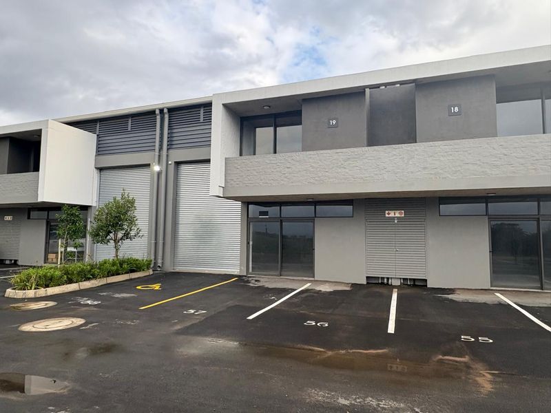 Modern industrial unit exterior featuring roller shutter doors, designated parking bays, and a contemporary grey concrete facade.