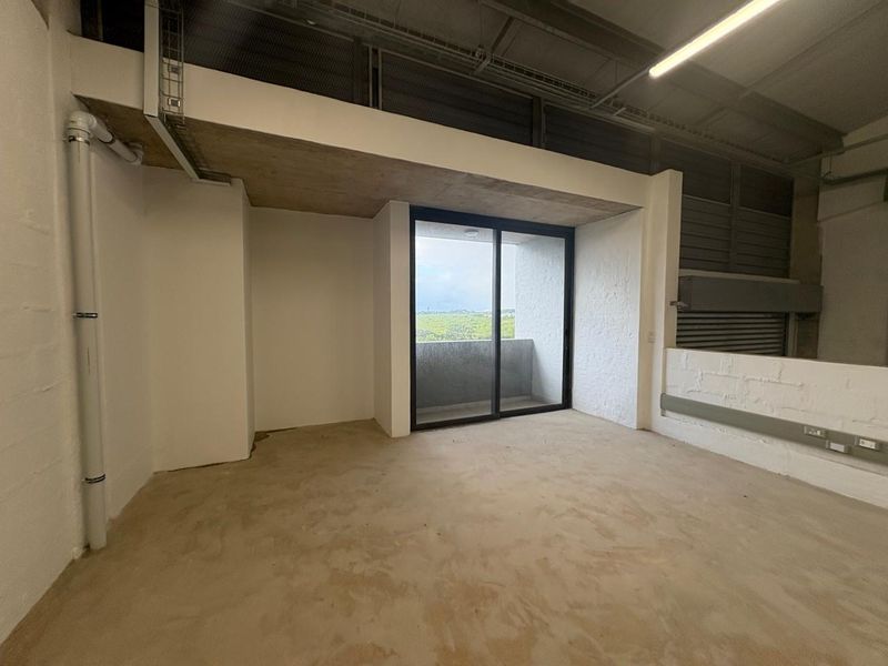 An industrial-style interior space featuring exposed ceilings, concrete flooring, and a sliding glass door leading to an outdoor area.