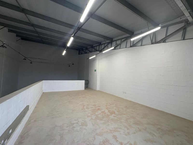 Spacious industrial utility area featuring exposed steel roof trusses, high ceilings, durable concrete flooring, and functional overhead strip lighting.
