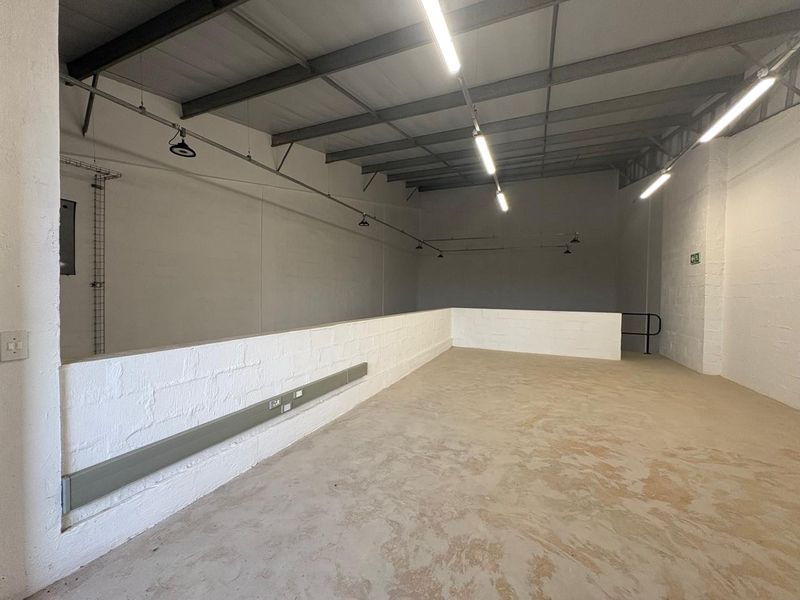 Spacious industrial utility area featuring exposed steel roof trusses, concrete flooring, and functional strip lighting, suitable for storage or workshop use.