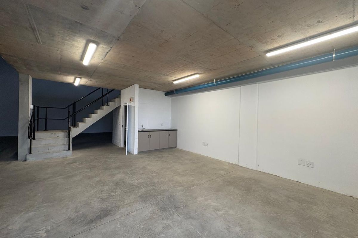 Spacious industrial utility area featuring exposed concrete ceilings, polished concrete floors, a staircase, and a compact kitchenette unit.