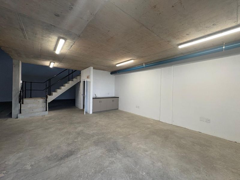 Spacious industrial utility area featuring exposed concrete ceilings, polished concrete floors, a staircase, and a compact kitchenette unit.