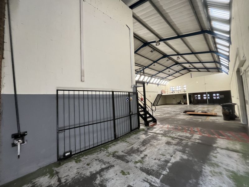 Spacious industrial warehouse featuring high ceilings with exposed steel trusses, skylights, concrete flooring, and a mezzanine level with staircase access.
