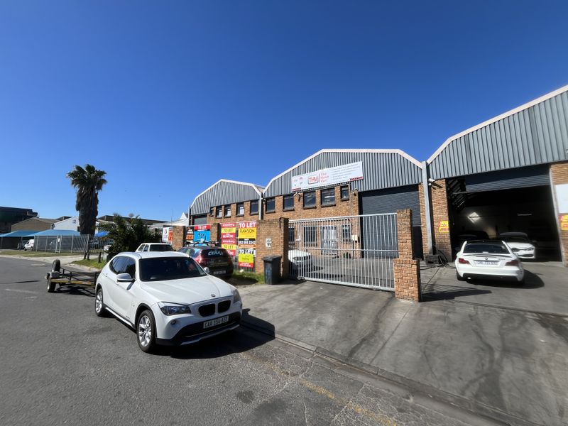 Front exterior view of an industrial warehouse property featuring brick construction, metal roofing, and secure gated access with roller shutter doors.
