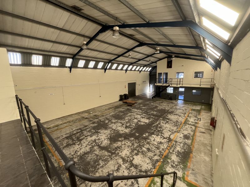 Spacious industrial warehouse featuring a mezzanine level, high-bay lighting, exposed steel trusses, and durable concrete flooring, suitable for various commercial or storage operations.