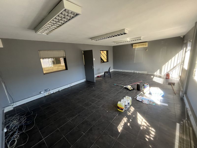 Spacious industrial office area featuring tiled flooring, fluorescent lighting, and a wall-mounted air conditioning unit, suitable for a professional workspace.
