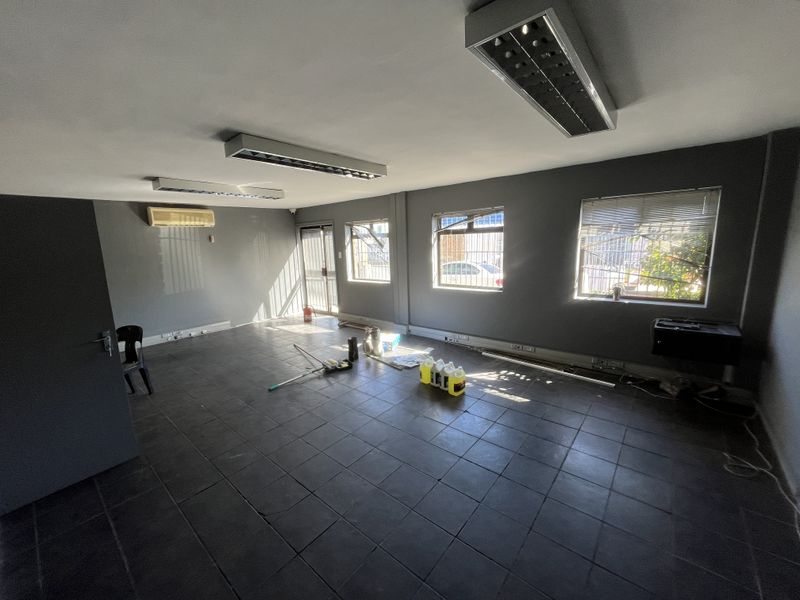 An empty industrial office space featuring tiled flooring, fluorescent lighting, split-system air conditioning, and windows with security bars.