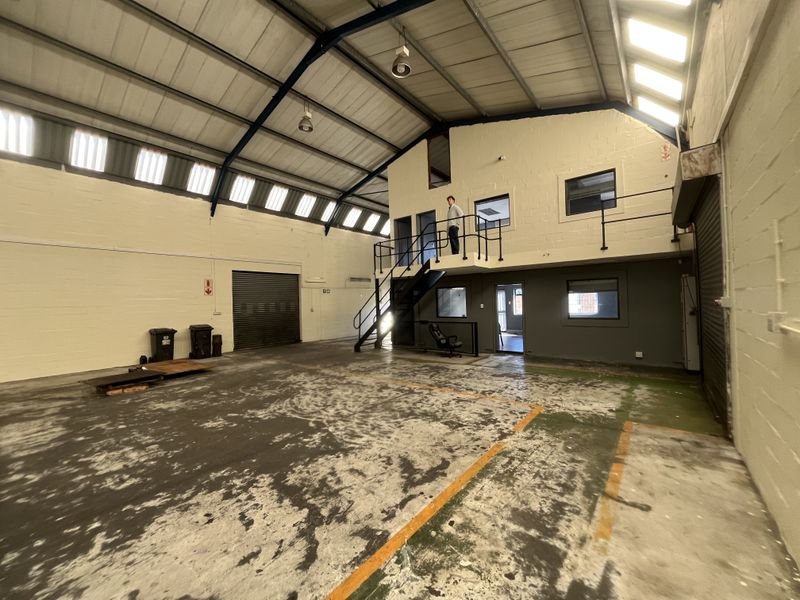 Spacious industrial warehouse unit featuring a mezzanine level, high ceilings with natural light panels, roller shutter access, and durable concrete flooring.