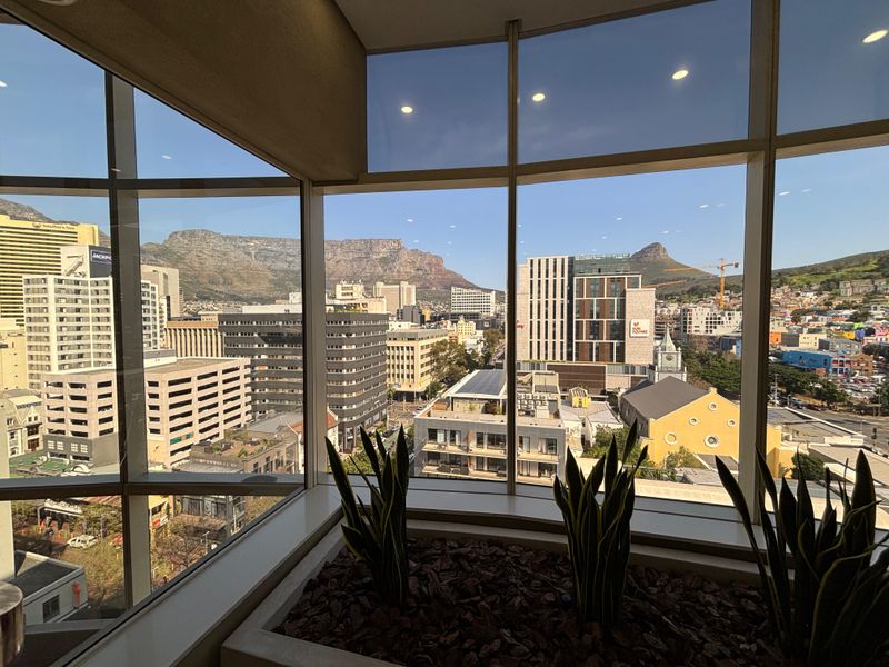 A high-level office space featuring expansive floor-to-ceiling windows with panoramic views of the city skyline and mountain range.