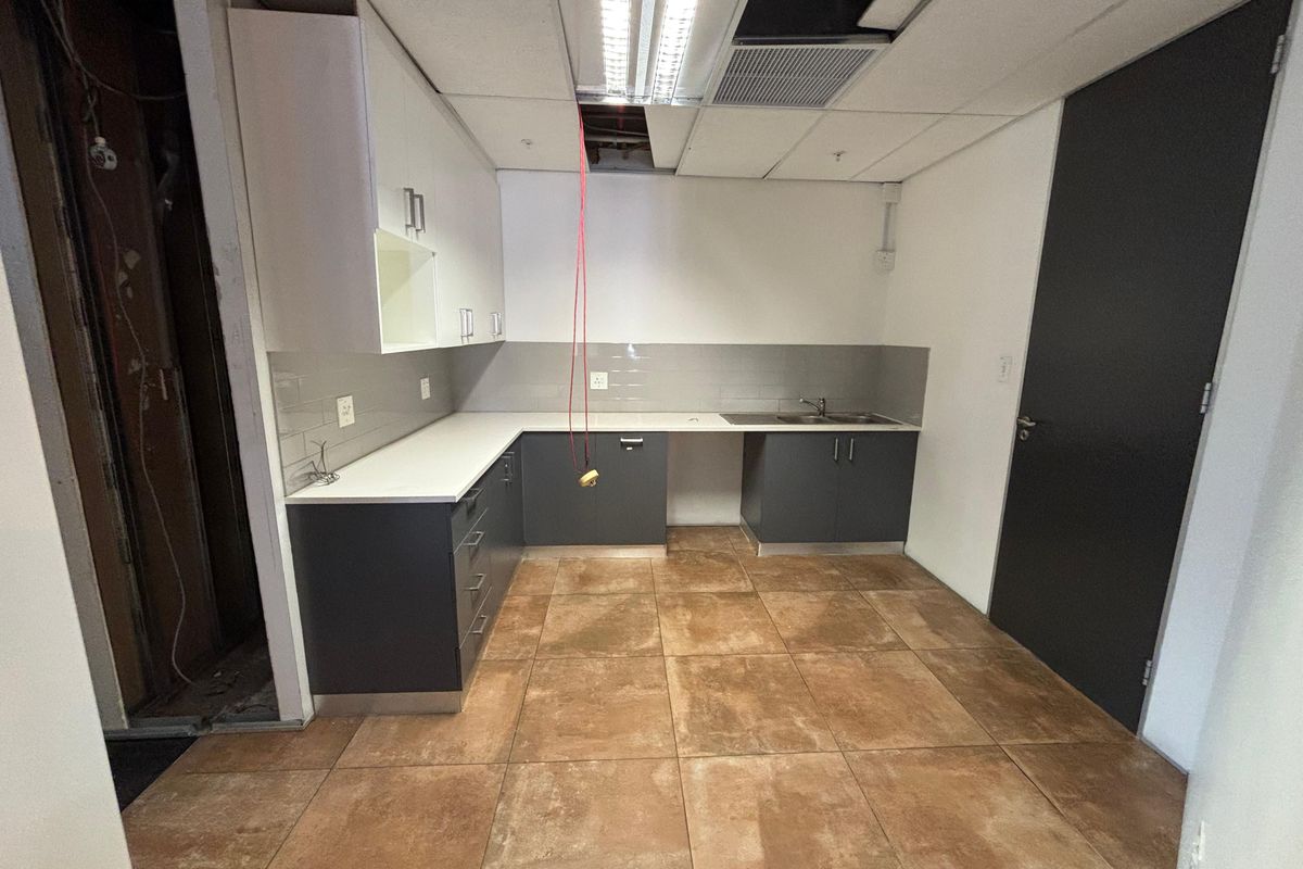 A small office kitchenette featuring dark base cabinets, white wall units, and tiled flooring, currently requiring ceiling and wall repairs.