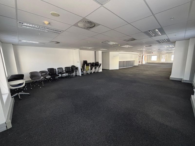A large, open-plan office space featuring a suspended ceiling, recessed lighting, integrated air conditioning, and fitted cabinetry along the rear wall.