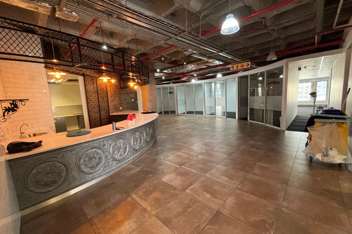 Modern open-plan office space featuring an industrial aesthetic with exposed ceilings, glass-partitioned offices, and a decorative built-in reception counter.