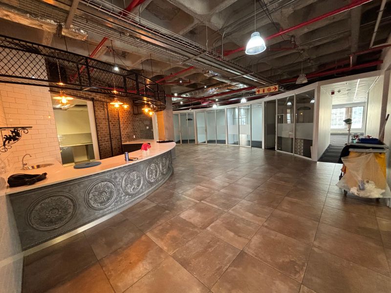 Modern open-plan office space featuring an industrial aesthetic with exposed ceilings, glass-partitioned offices, and a decorative built-in reception counter.
